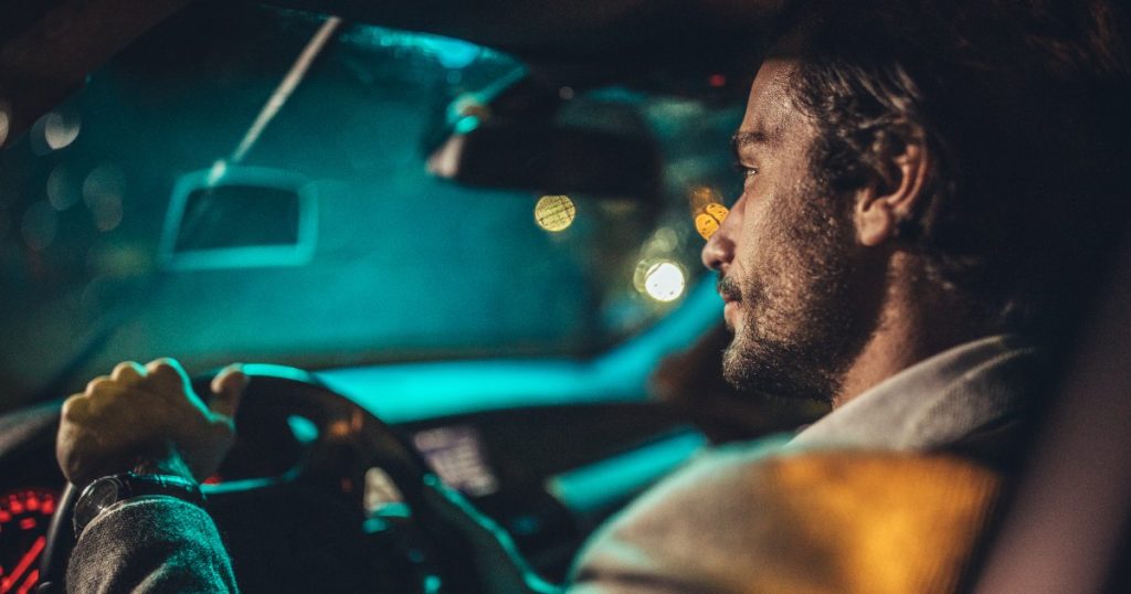 Current image: bearded young male driver in car at night